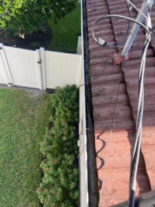 gutter cleaning service performed on a roof with tiles showing greenery and a fence in the background